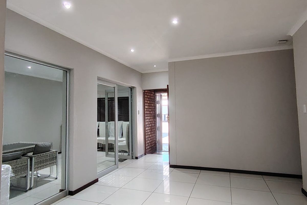 Spacious living area featuring neutral tiled flooring, recessed downlighting, and sliding glass doors leading to an adjacent room with exposed brick accents.