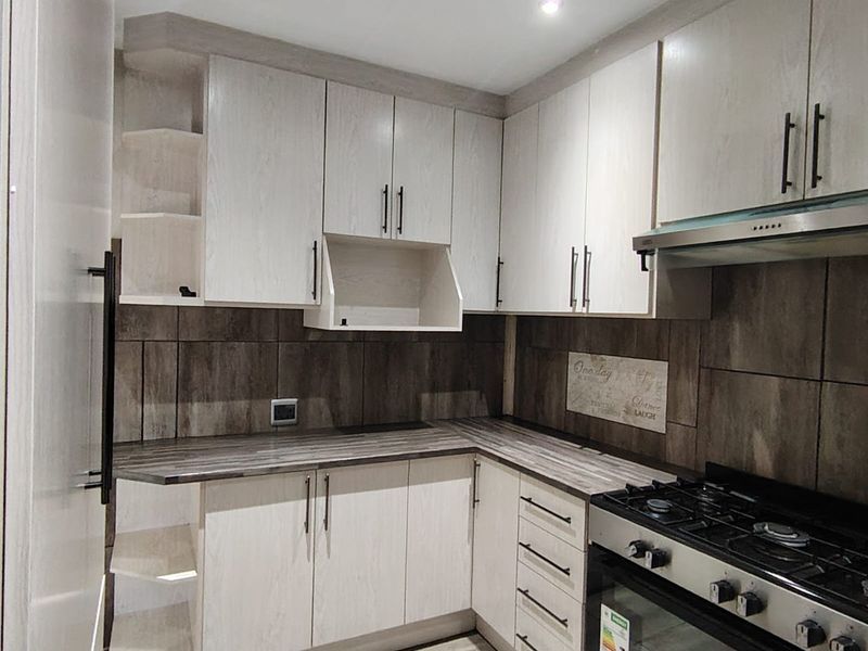 Modern kitchen featuring light wood-grain cabinetry, dark laminate countertops, tiled backsplash, and a built-in gas stove with an integrated extractor fan.