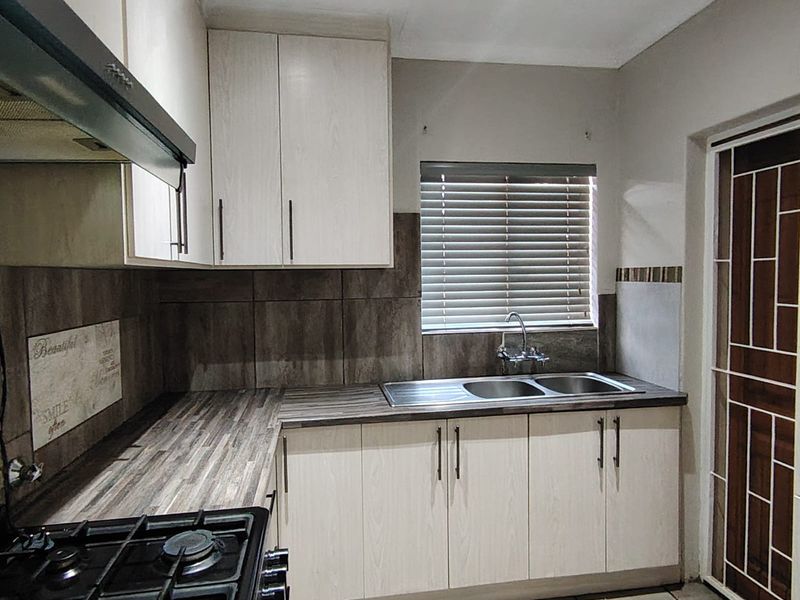 A functional kitchen featuring light wood-grain cabinetry, dark laminate countertops, a gas hob with extractor, and tiled finishes throughout.