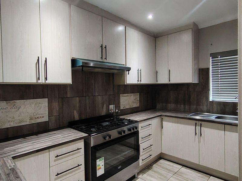 Modern kitchen featuring light wood-grain cabinetry, dark tiled backsplash, gas stove with extractor, and durable tiled flooring.