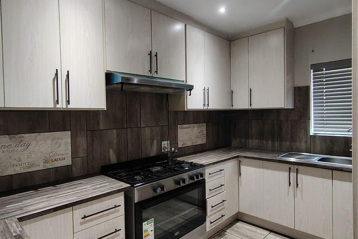 Modern kitchen featuring light wood-grain cabinetry, dark tiled backsplash, gas stove with extractor, and durable tiled flooring.