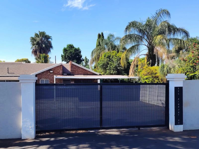 Front view of the property featuring a secure sliding gate, perimeter wall, and a brick facade house with a tiled roof.