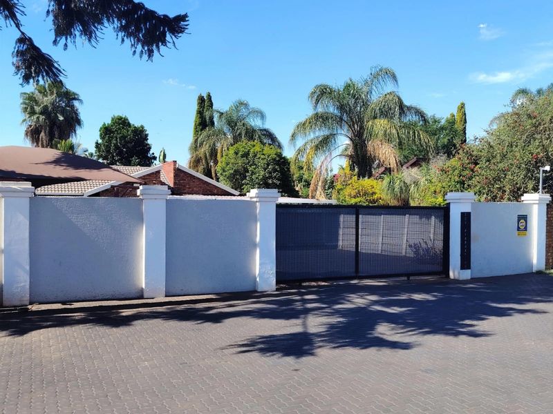 Front view of the property featuring a secure perimeter wall, a modern sliding gate, and a paved driveway entrance.