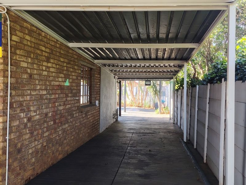 A covered carport area featuring a brick side wall, paved driveway, and precast concrete boundary wall.