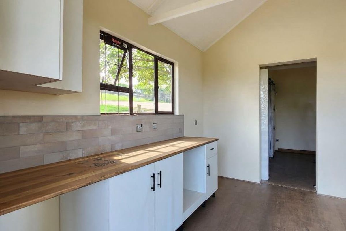 A bright, modern kitchen area featuring white cabinetry, a warm timber countertop, subway tile backsplash, and a high vaulted ceiling with exposed trusses.