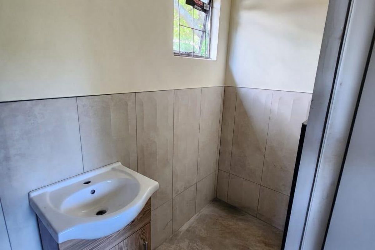 A compact bathroom featuring a modern vanity cabinet with a ceramic basin, neutral wall tiling, and tiled flooring.
