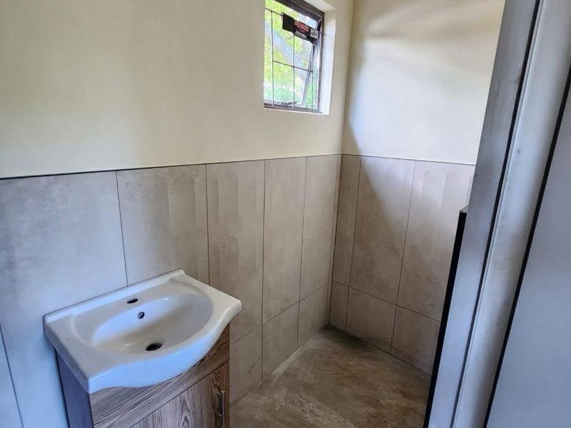 A compact bathroom featuring a modern vanity cabinet with a ceramic basin, neutral wall tiling, and tiled flooring.