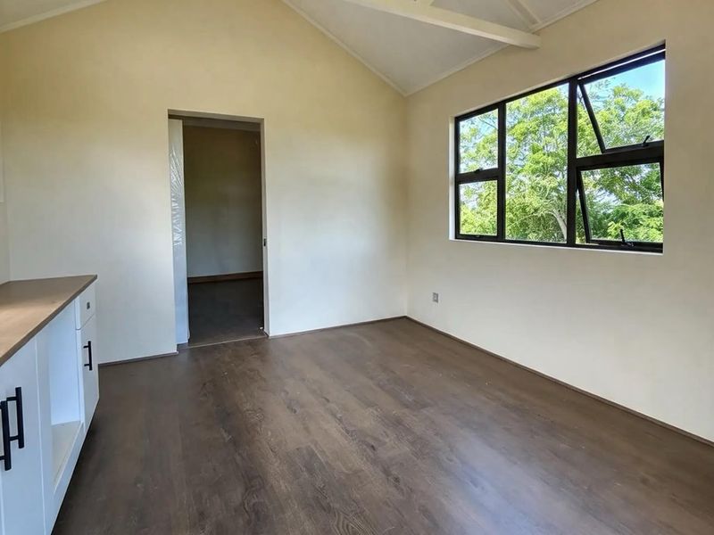 Bright open-plan living area featuring vaulted ceilings with exposed trusses, modern laminate flooring, and large windows providing natural light.