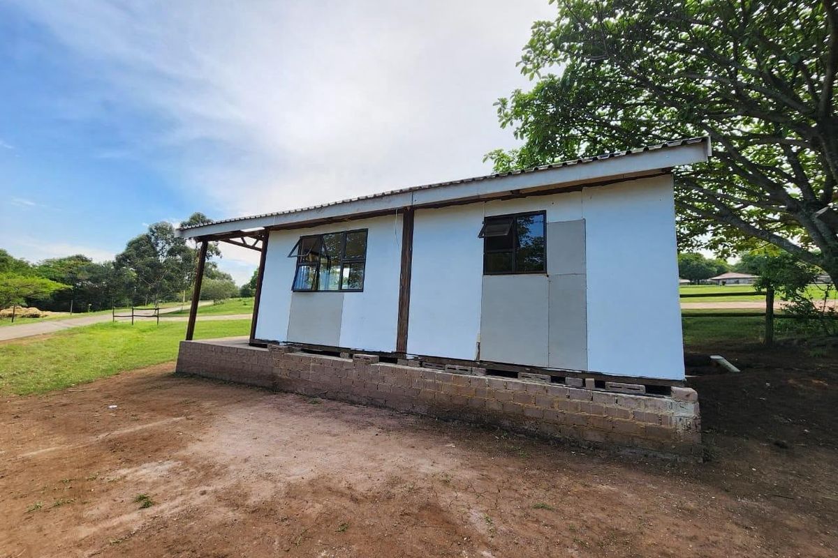Rear view of a cottage structure featuring a corrugated metal roof, aluminium windows, and an unfinished exterior wall finish on a raised concrete block foundation.
