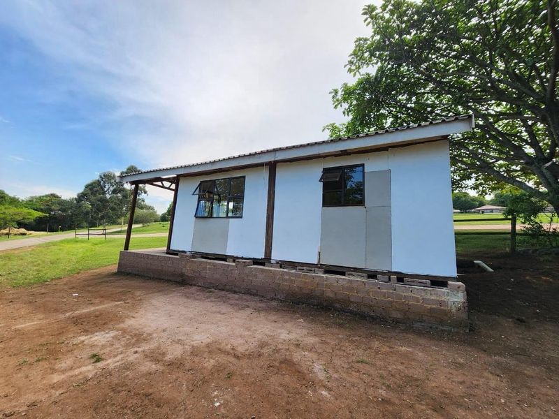 Rear view of a cottage structure featuring a corrugated metal roof, aluminium windows, and an unfinished exterior wall finish on a raised concrete block foundation.