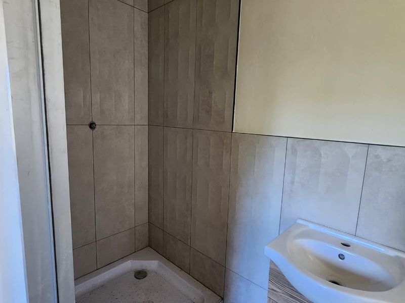 A compact bathroom featuring a shower enclosure with tiled walls and a modern vanity basin with storage cabinet.