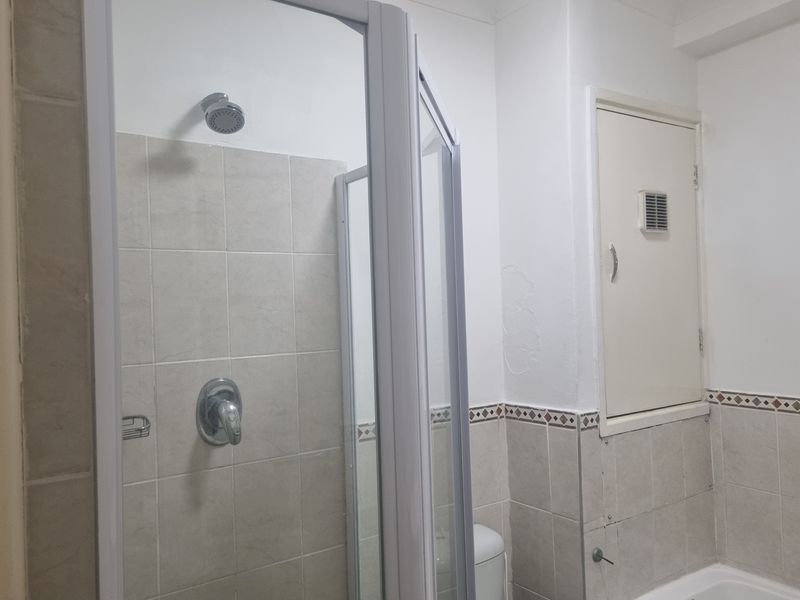 A functional bathroom featuring a shower enclosure with tiled walls and a built-in wall cupboard, showing signs of wear on the wall surfaces.