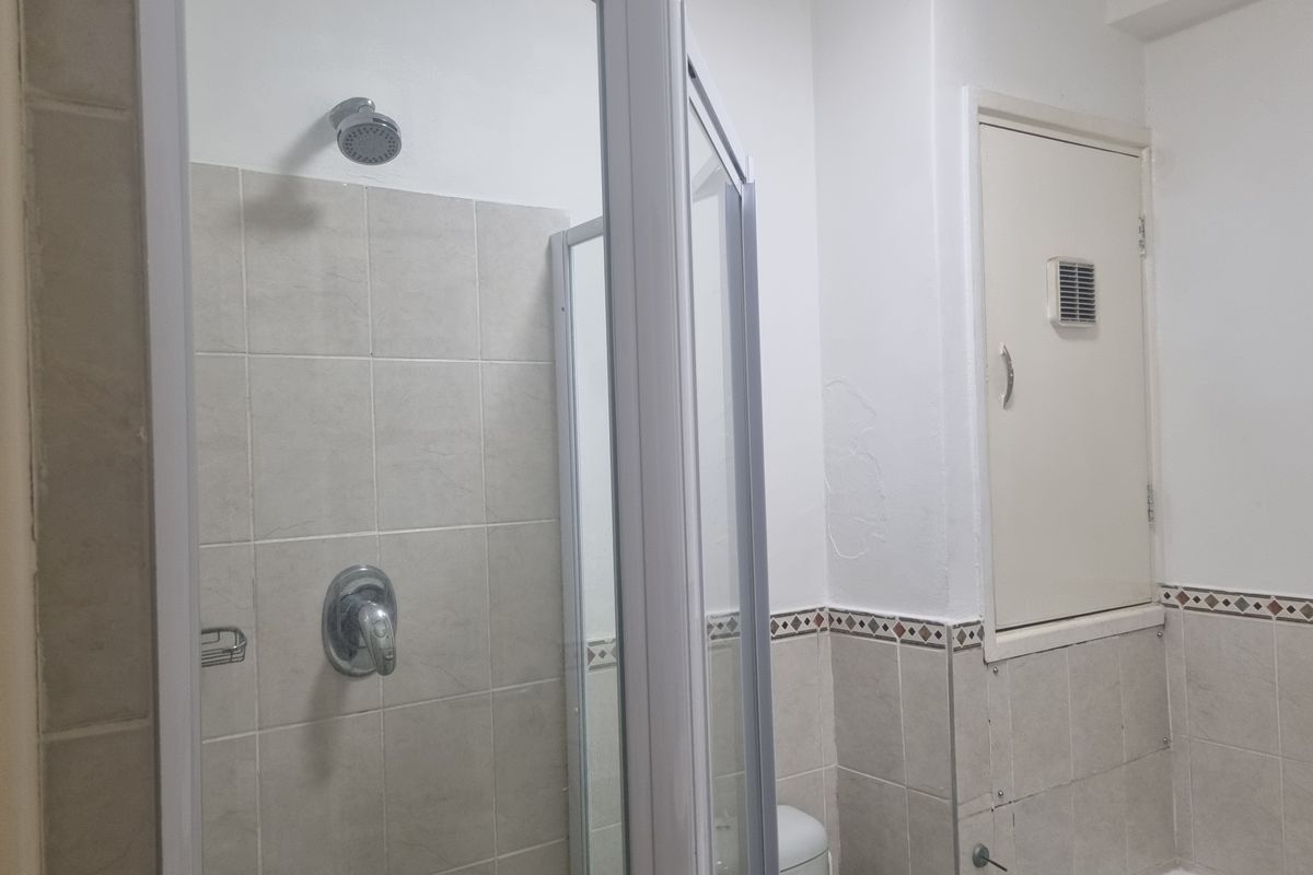 A functional bathroom featuring a shower enclosure with tiled walls and a built-in wall cupboard, showing signs of wear on the wall surfaces.