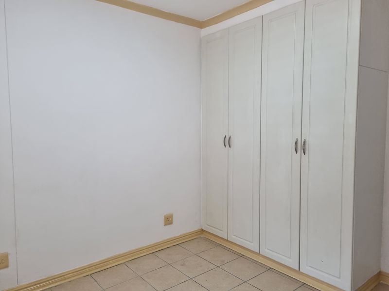 A clean, empty bedroom featuring neutral tiled flooring and ample built-in cupboard storage space.