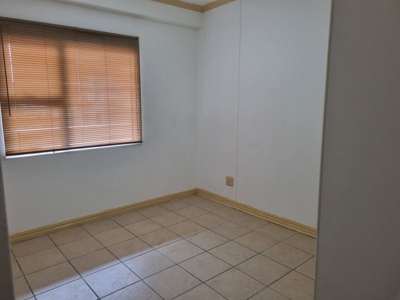 An empty bedroom featuring neutral tiled flooring, white walls, and fitted venetian blinds, offering a blank canvas for personalization.