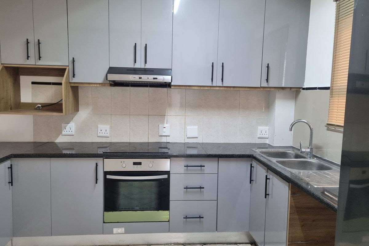 Modern kitchen featuring grey cabinetry, granite countertops, built-in oven, electric hob, extractor fan, and a double bowl sink with tiled backsplash.