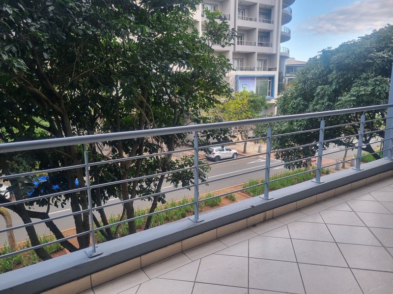 A clean, tiled balcony featuring a modern metal balustrade overlooking the street and surrounding trees.