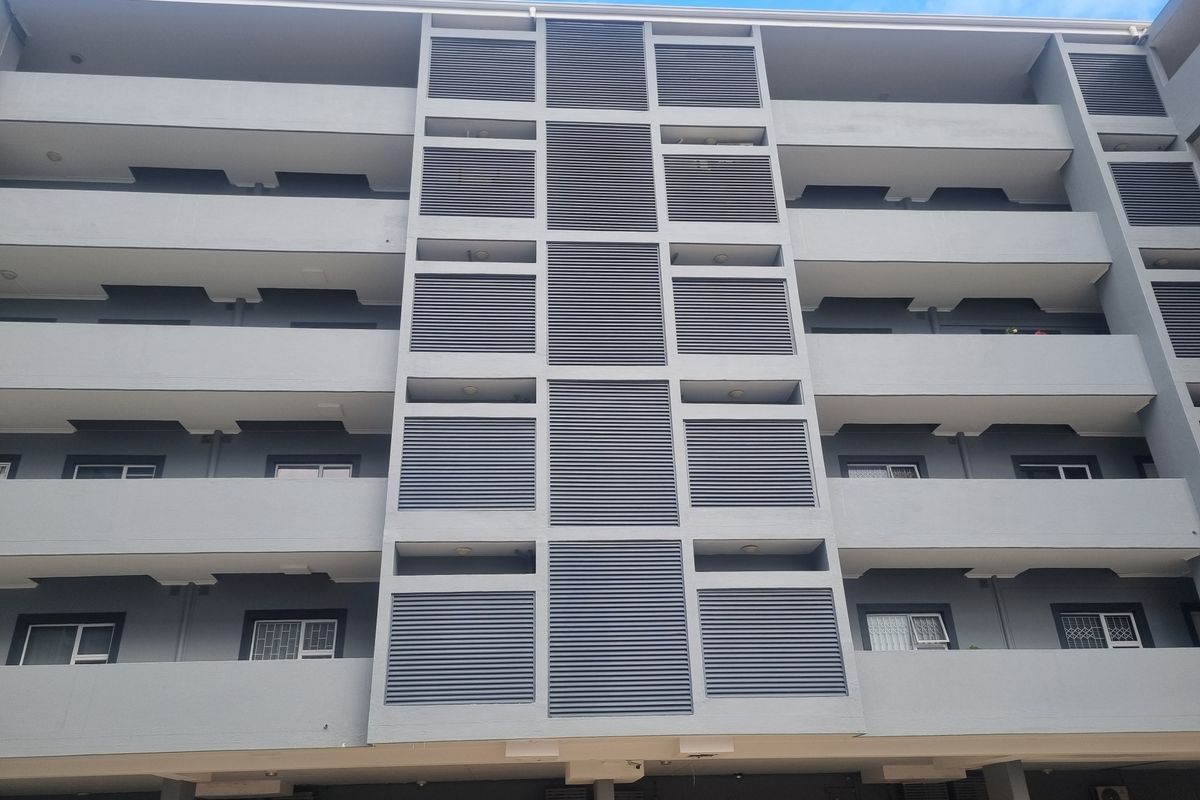 A view of the apartment building facade featuring multiple levels of balconies with grey louvre privacy screens and security-fitted windows.