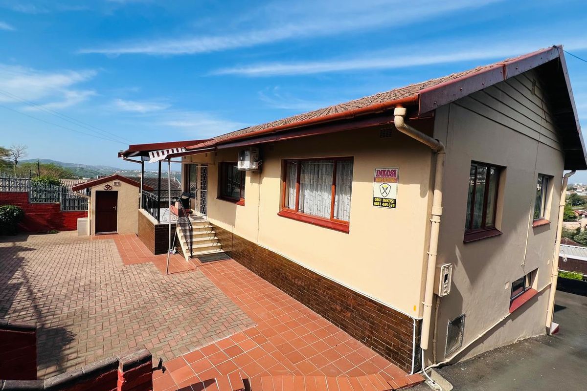 Rear exterior view of the house featuring paved courtyard, tiled roof, and secure access points with external air conditioning unit.