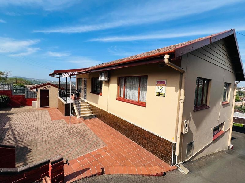 Rear exterior view of the house featuring paved courtyard, tiled roof, and secure access points with external air conditioning unit.