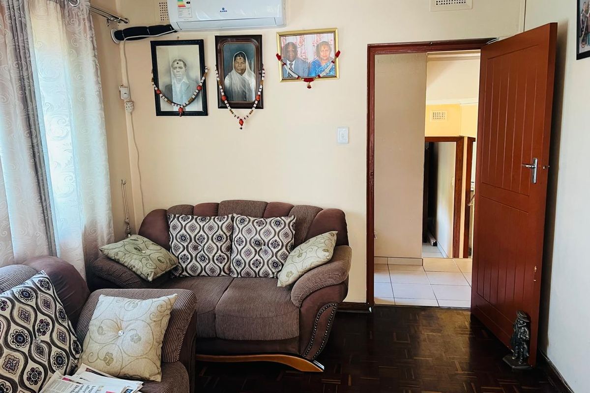 A living room featuring parquet flooring, a split-system air conditioner, and a timber door leading to an adjacent hallway.