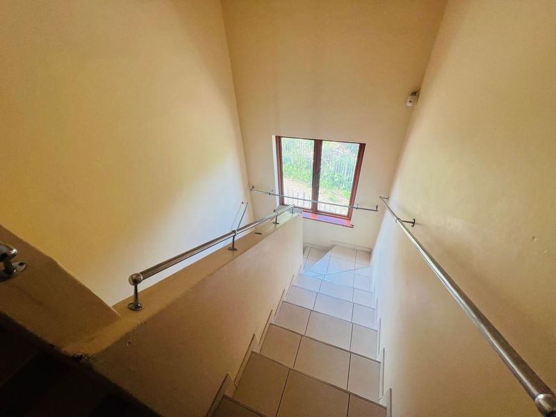 A bright, tiled staircase featuring stainless steel handrails and a window providing natural light.