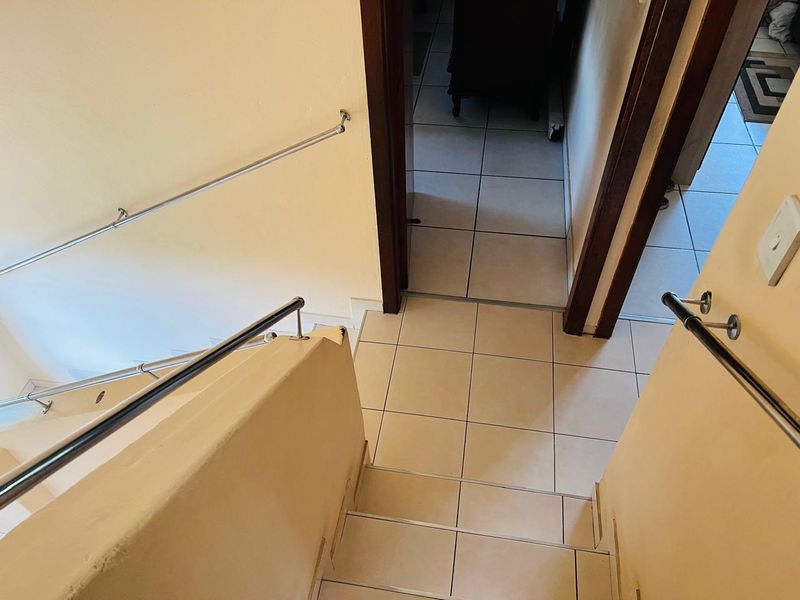 A functional hallway and staircase area featuring tiled flooring and metal handrails, providing access to adjacent rooms.