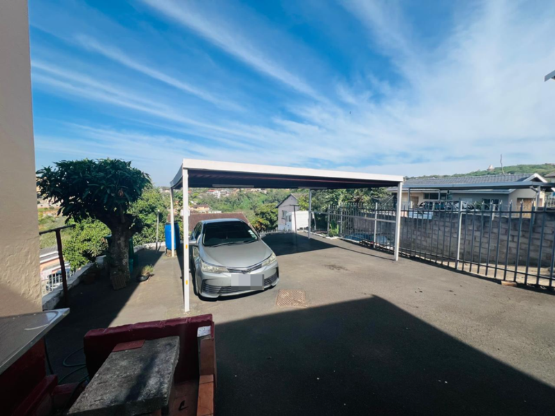 Rear exterior area featuring a paved driveway, a functional carport structure, and secure metal perimeter fencing.