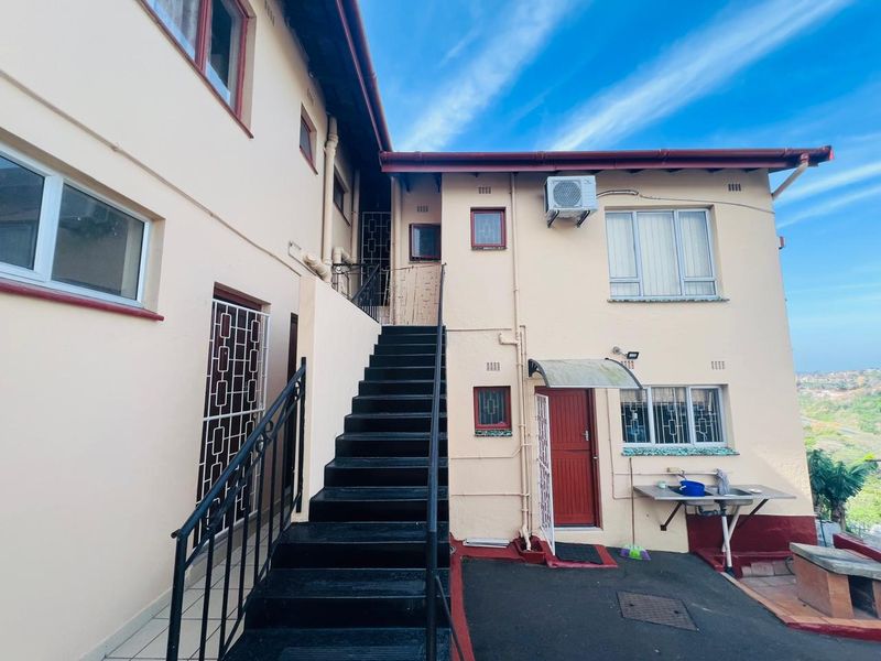 Rear exterior view of the property featuring an external staircase, security gates, and a functional outdoor sink area with paved patio space.