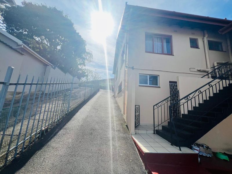 Exterior view of the property featuring an asphalt driveway, metal security fencing, and an external staircase leading to the entrance.