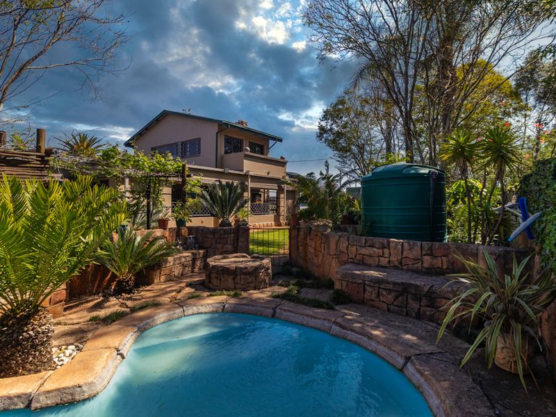 A landscaped rear garden area featuring a swimming pool, stone retaining walls, a built-in fire pit, and a water storage tank.