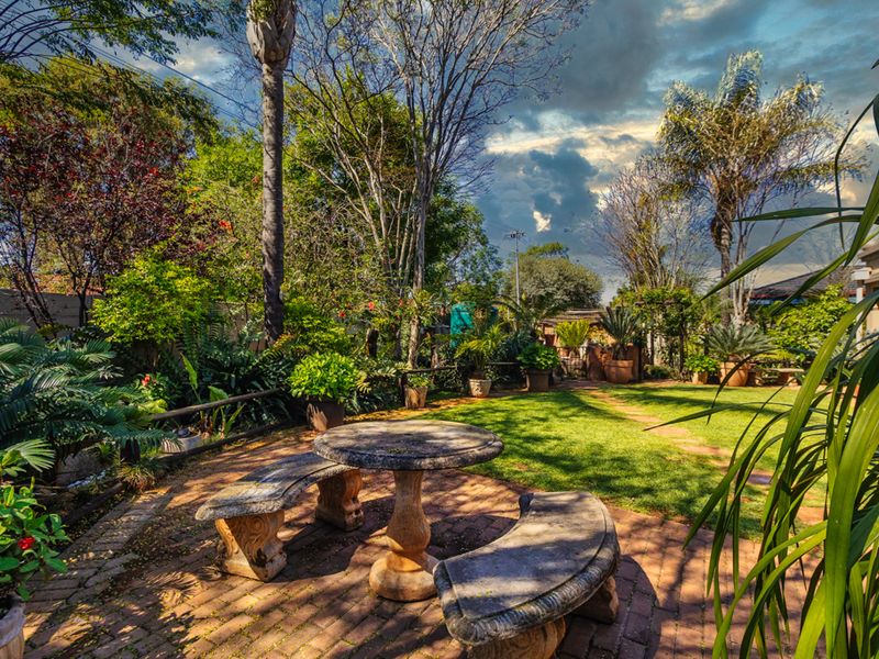 A lush, well-established garden featuring mature trees, manicured lawn, and a paved seating area, providing a tranquil outdoor space.