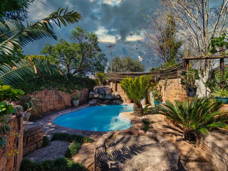 A landscaped outdoor pool area featuring natural stone cladding, a rock water feature, and established garden surroundings.