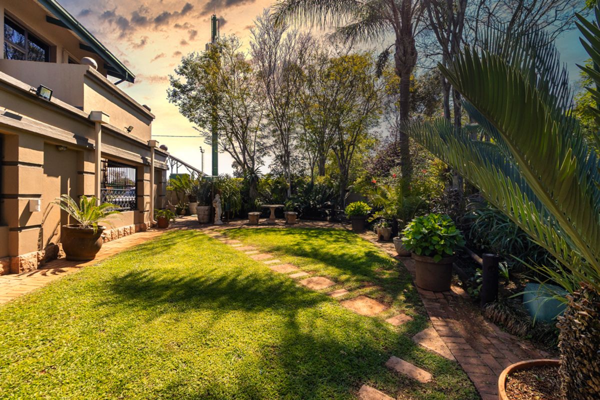 A well-maintained rear garden featuring a lush lawn, paved pathways, and established landscaping adjacent to the house exterior.
