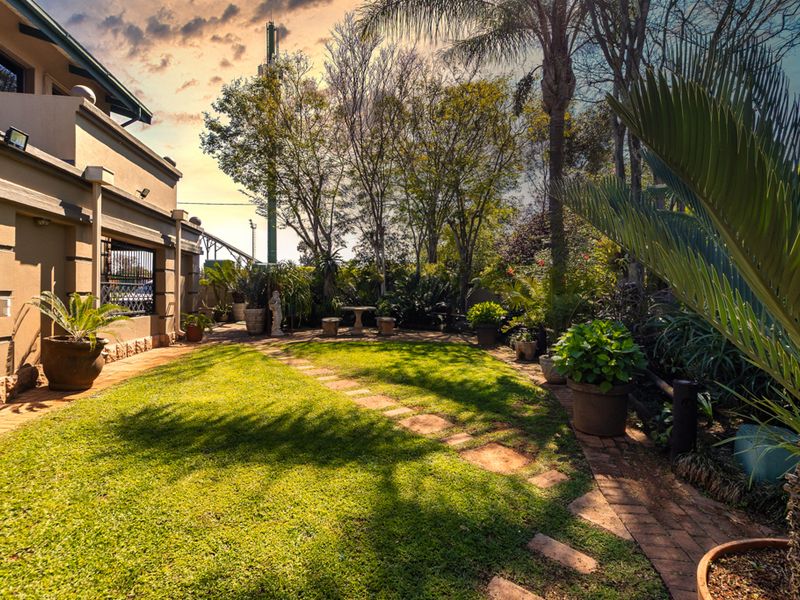 A well-maintained rear garden featuring a lush lawn, paved pathways, and established landscaping adjacent to the house exterior.