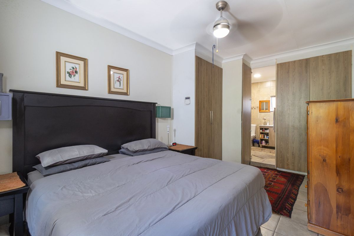 A bedroom featuring built-in cupboards, a ceiling fan, and direct access to an en-suite bathroom with tiled flooring throughout.