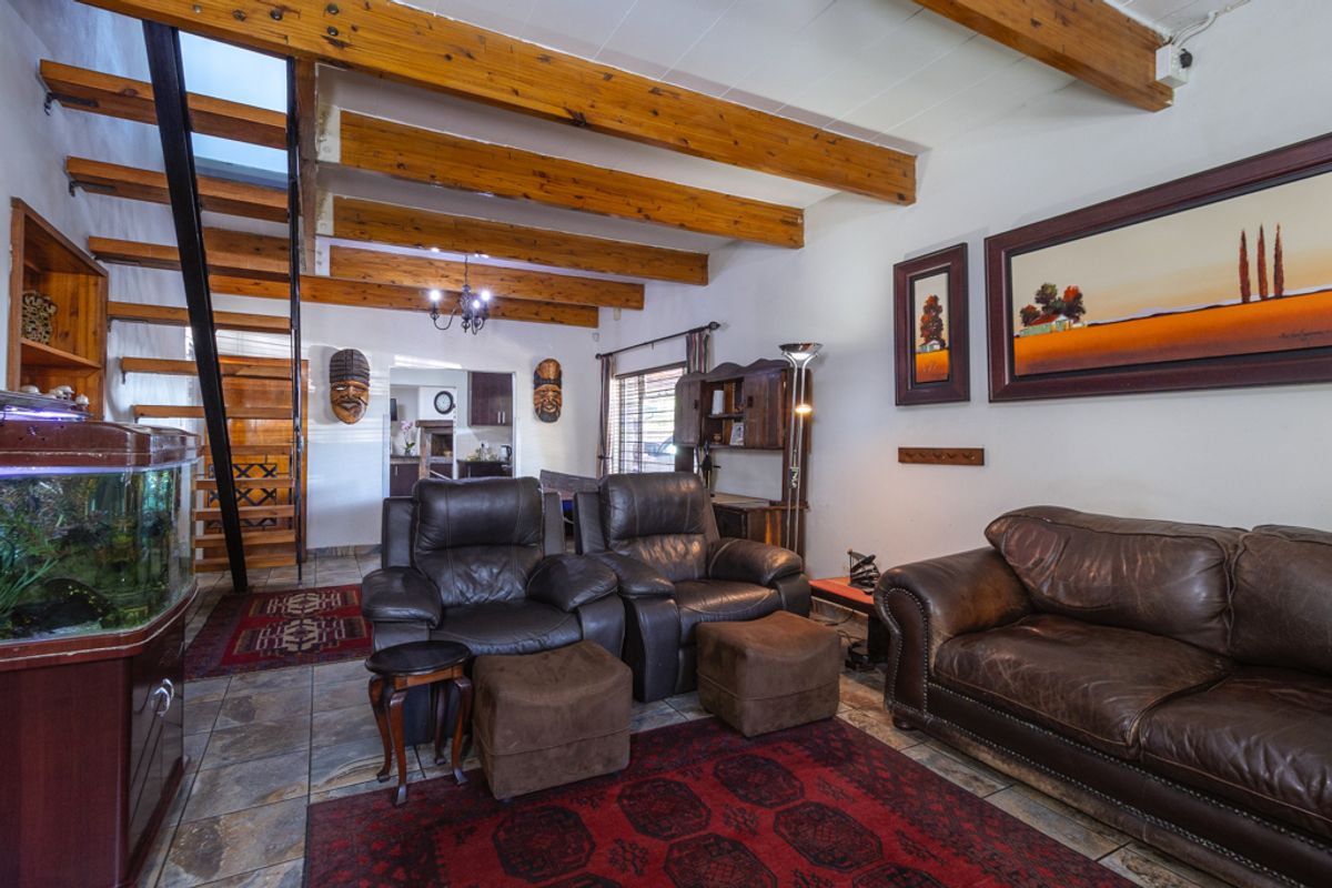 Spacious living area featuring exposed timber ceiling beams, tiled flooring, and a wooden staircase leading to the upper level.