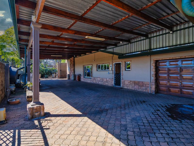 A spacious covered carport area featuring timber support columns, stone cladding accents, and a secure garage entrance with paved flooring.