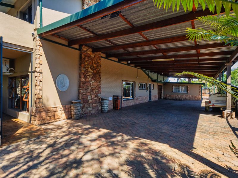 Spacious paved driveway featuring a large covered carport with timber beams and stone-clad exterior wall detailing.