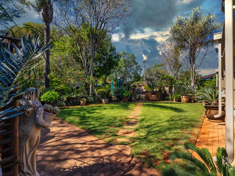 A well-maintained garden featuring a lush green lawn, mature trees, and a brick-paved walkway leading through the landscaped outdoor space.