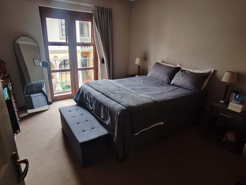 A comfortable bedroom featuring carpet flooring, a ceiling fan, and double doors leading to a small balcony.