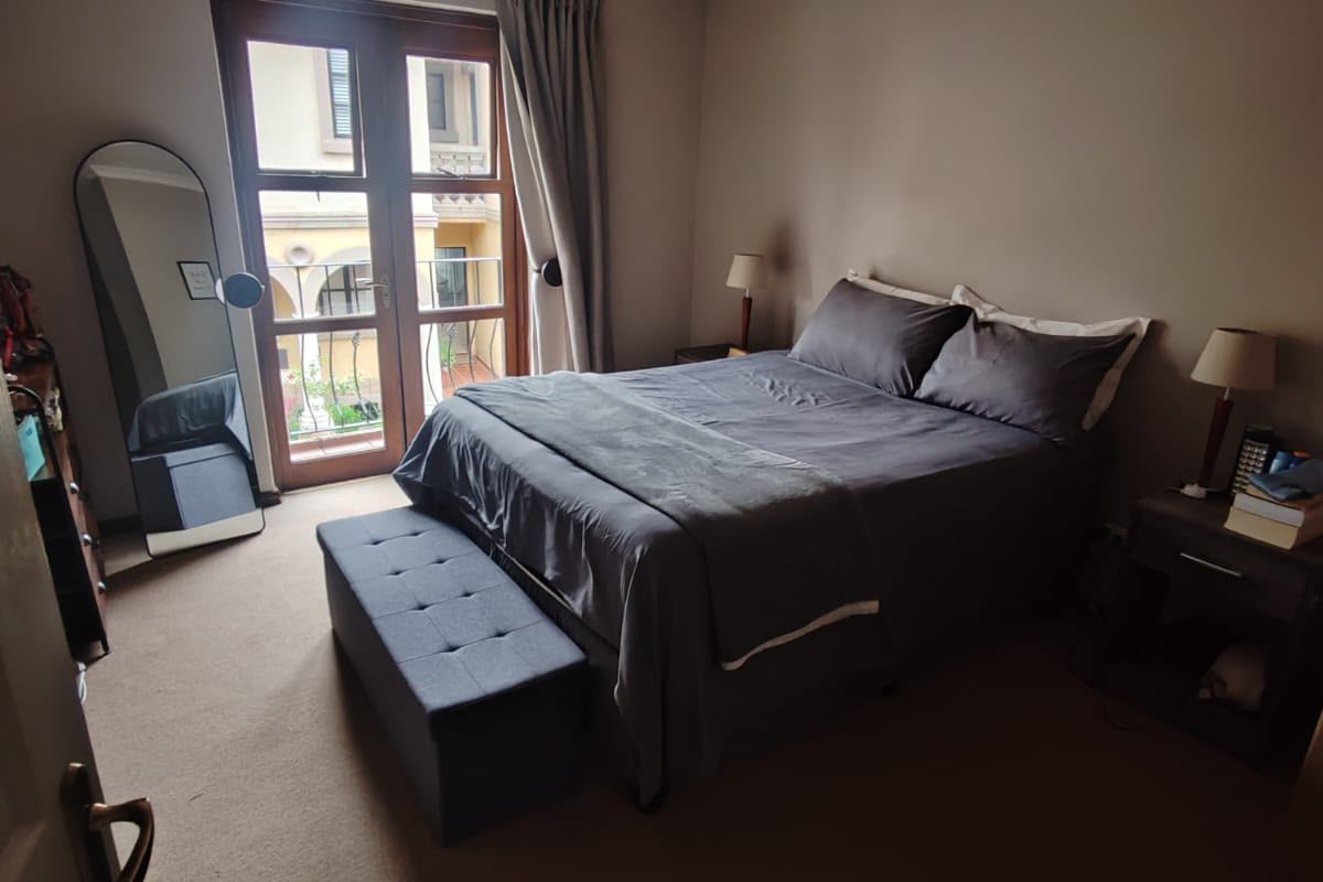 A comfortable bedroom featuring carpet flooring, a ceiling fan, and double doors leading to a small balcony.