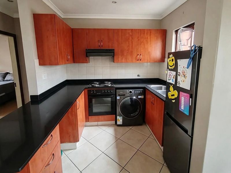 A functional kitchen featuring wood-finish cabinetry, black countertops, a built-in oven with gas hob, and tiled flooring with integrated laundry appliance space.