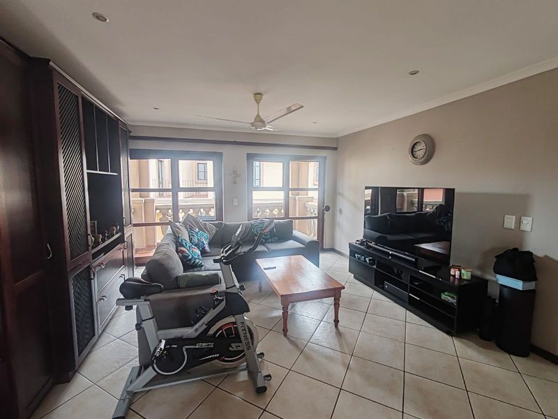 A spacious living room featuring tiled flooring, recessed lighting, a ceiling fan, and built-in cabinetry, with direct access to a balcony through sliding glass doors.