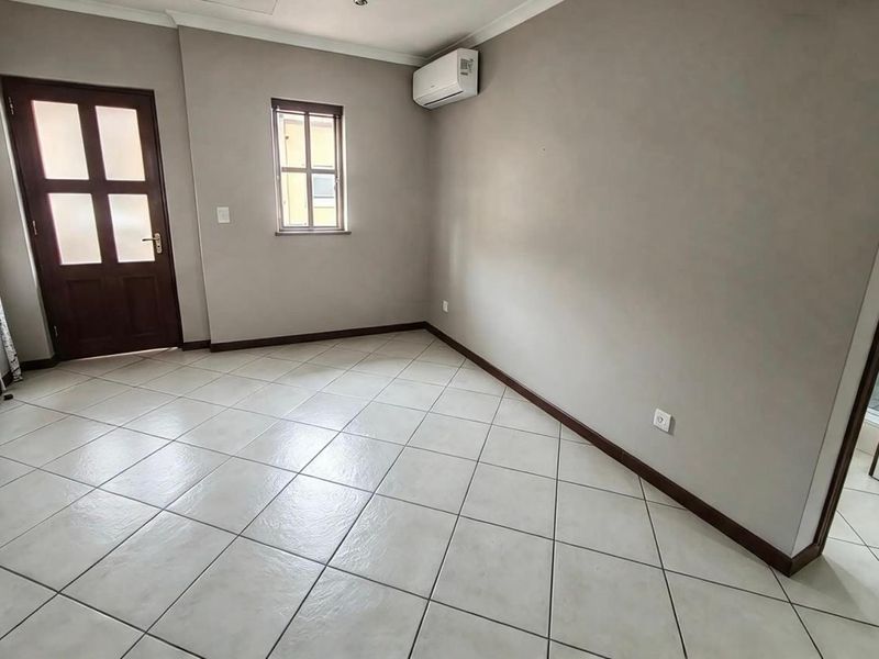 A bright, empty living area featuring neutral tiled flooring, a wall-mounted air conditioning unit, and a classic timber door.