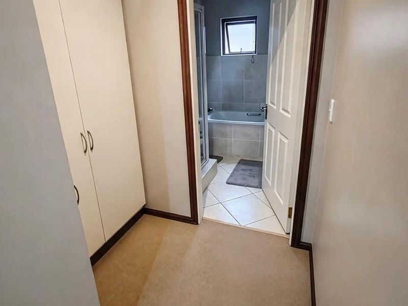 A carpeted hallway featuring built-in storage cupboards, leading directly into a tiled bathroom with a bathtub.