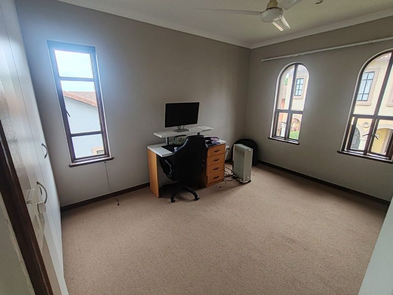 A spacious bedroom featuring neutral carpeting, built-in cupboards, a ceiling fan, and distinctive arched windows providing natural light.