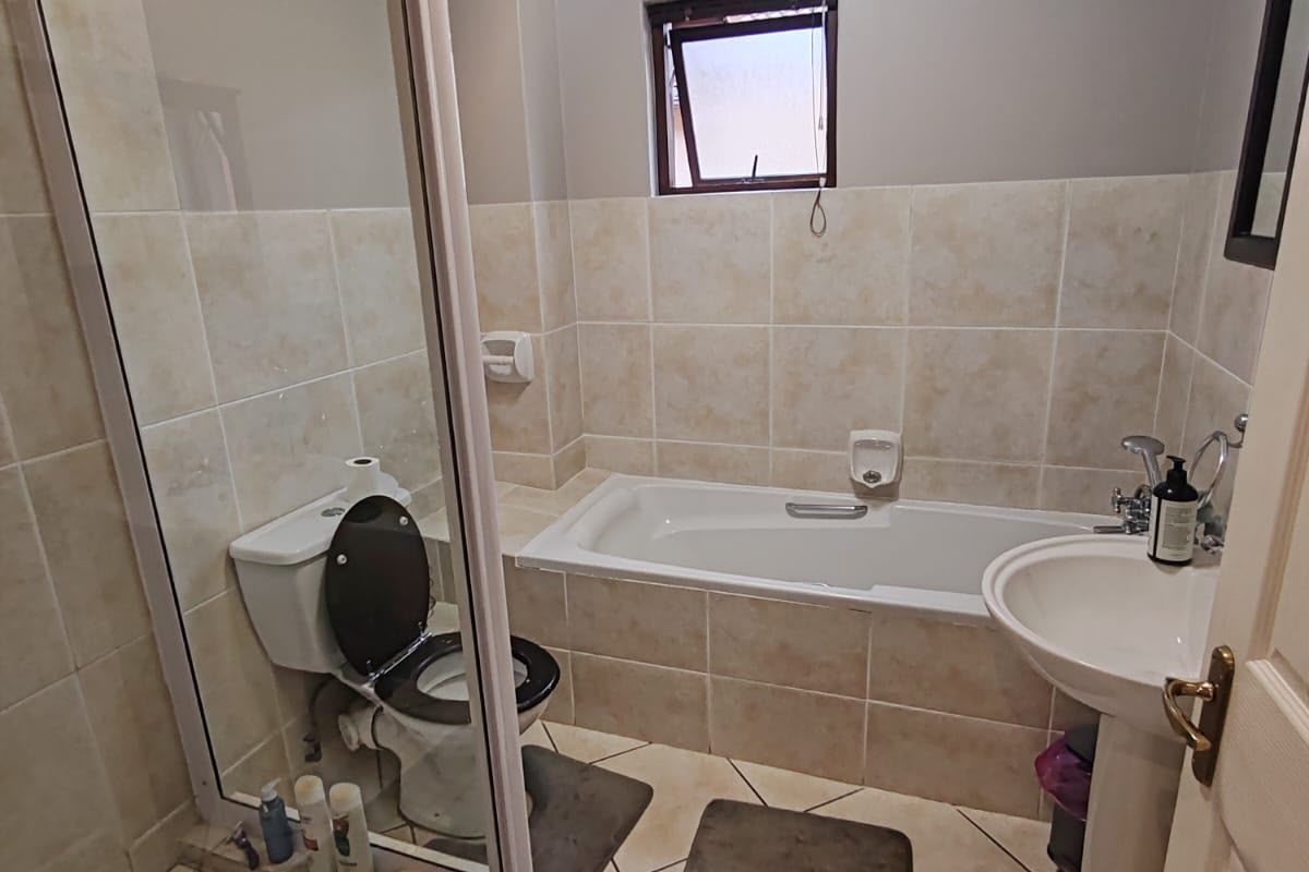 A functional bathroom featuring a shower enclosure, bathtub, pedestal sink, and toilet with neutral tiled finishes.