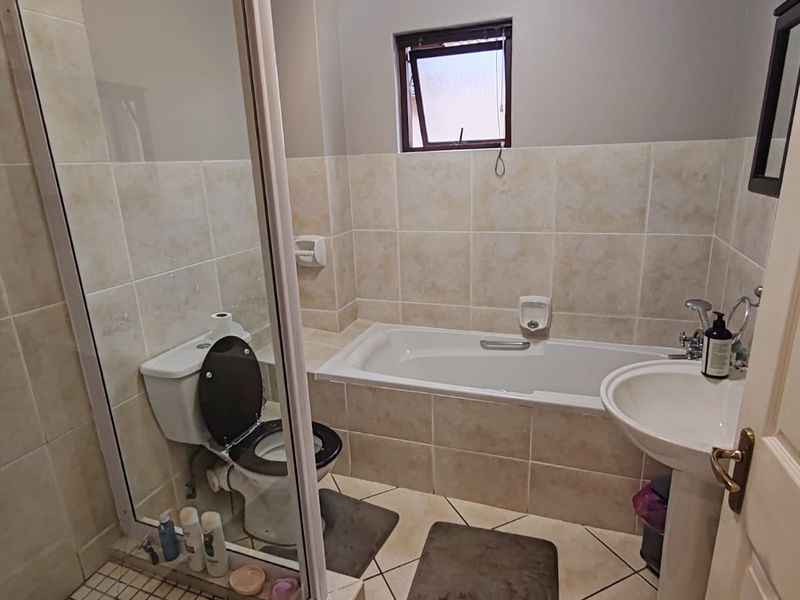 A functional bathroom featuring a shower enclosure, bathtub, pedestal sink, and toilet with neutral tiled finishes.