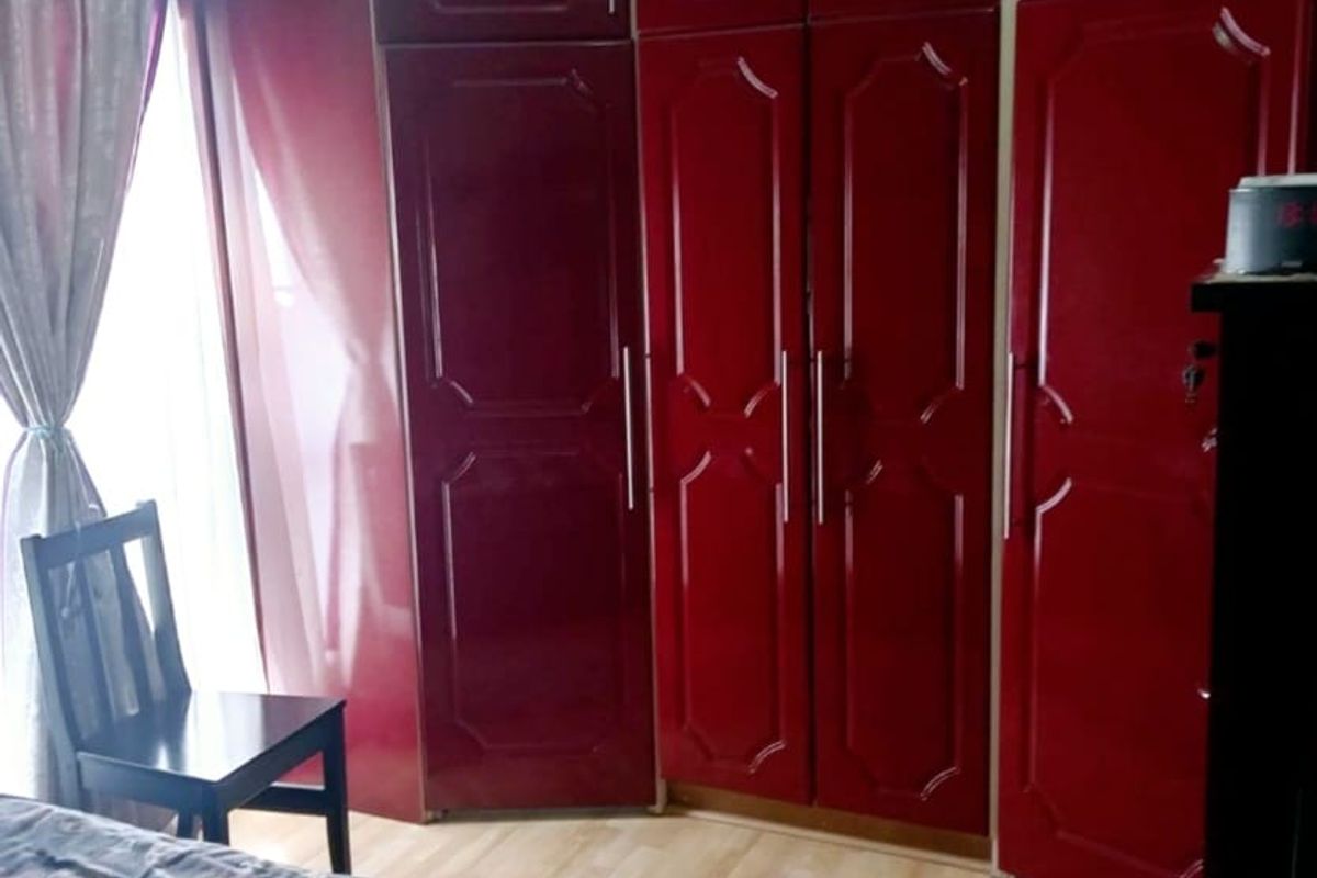 A bedroom featuring floor-to-ceiling built-in cupboards with a high-gloss red finish and light wood-look flooring.